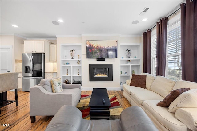 living room featuring light wood-style flooring, recessed lighting, visible vents, ornamental molding, and a glass covered fireplace