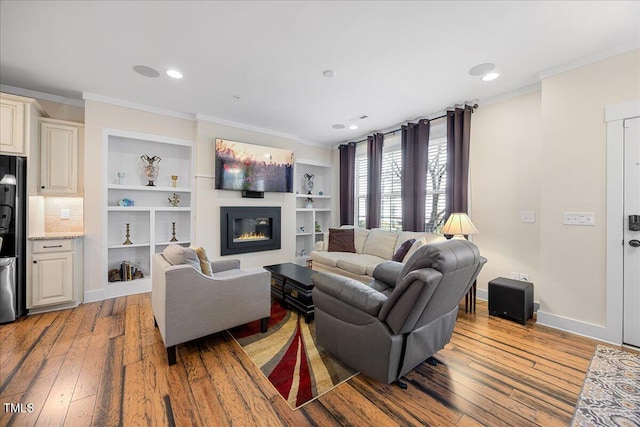 living area featuring ornamental molding, a glass covered fireplace, light wood-style flooring, and baseboards