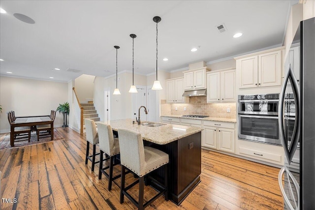 kitchen featuring under cabinet range hood, ornamental molding, stainless steel appliances, and a sink