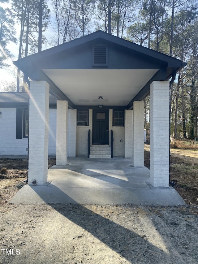 property entrance featuring dirt driveway, an attached carport, and brick siding