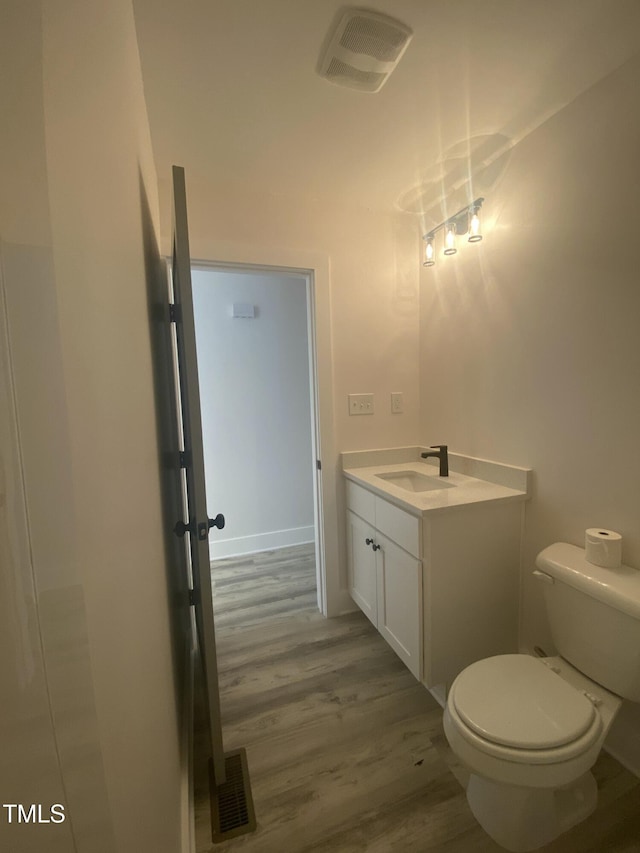 half bath with visible vents, toilet, wood finished floors, and vanity