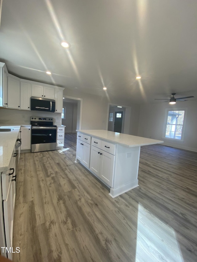 kitchen with stainless steel appliances, white cabinets, a kitchen island, and light wood-style flooring