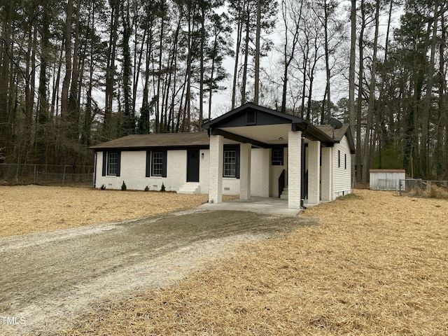 view of front of property featuring brick siding, an attached carport, driveway, and fence