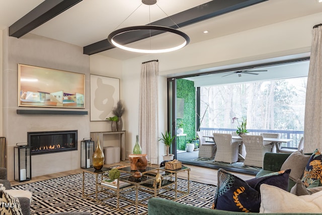 living area with beam ceiling, a glass covered fireplace, a wealth of natural light, and wood finished floors