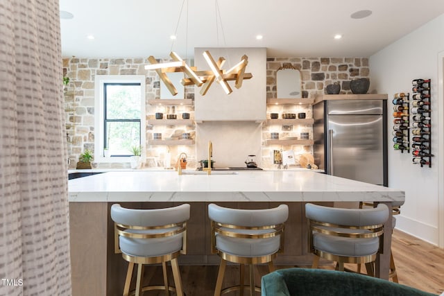 kitchen featuring stainless steel built in fridge, a large island, light wood-style flooring, light stone counters, and recessed lighting