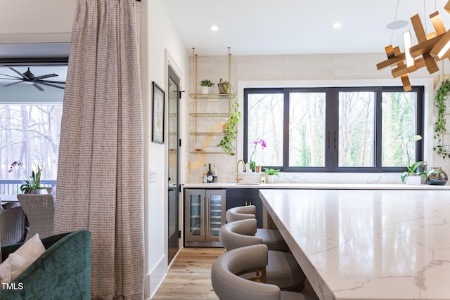 bar featuring wine cooler, indoor wet bar, light wood-style floors, a ceiling fan, and a sink