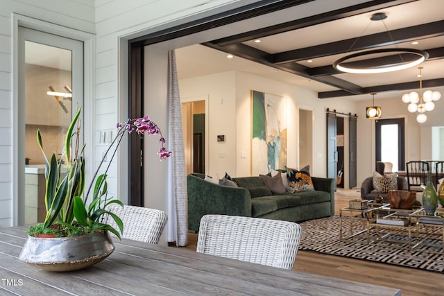 living area with a chandelier, beamed ceiling, a barn door, and wood finished floors