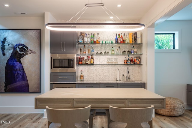 bar with indoor wet bar, stainless steel microwave, light wood finished floors, and a sink