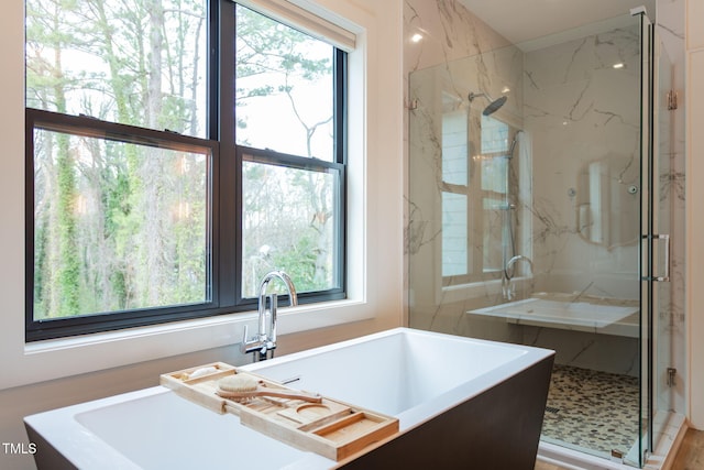 bathroom with a marble finish shower and a freestanding bath