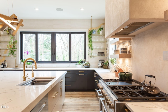 kitchen featuring custom range hood, a sink, light stone counters, stainless steel stove, and light wood finished floors