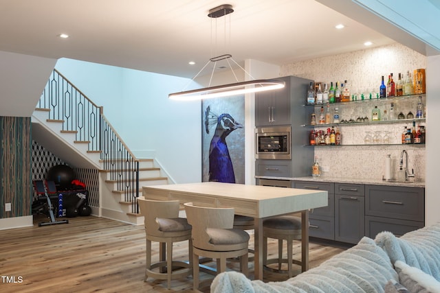 bar with stainless steel microwave, stairs, indoor wet bar, light wood-style floors, and a sink