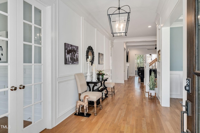 foyer entrance with light wood-style floors, a decorative wall, crown molding, and french doors