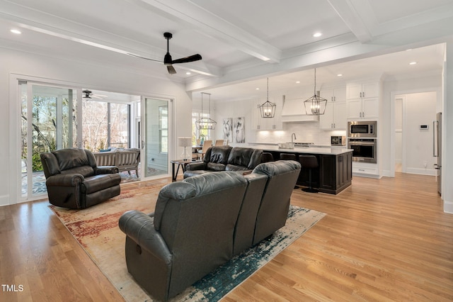 living area featuring ornamental molding, light wood-type flooring, beamed ceiling, baseboards, and ceiling fan with notable chandelier