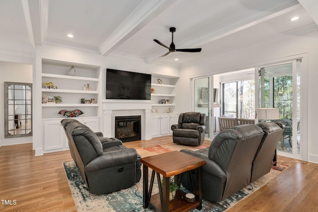 living area with built in features, recessed lighting, light wood-style flooring, a glass covered fireplace, and beamed ceiling