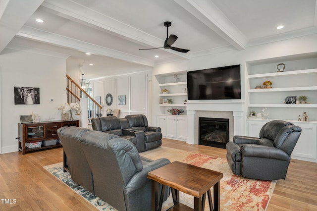 living area featuring light wood finished floors, stairs, beamed ceiling, and a glass covered fireplace