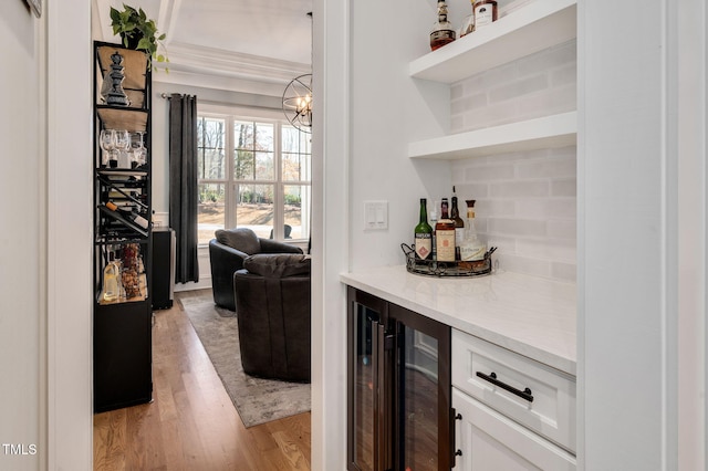 bar featuring a notable chandelier, a dry bar, light wood-style flooring, backsplash, and beverage cooler