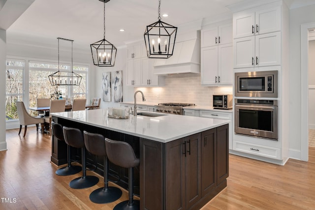 kitchen with a sink, light countertops, appliances with stainless steel finishes, custom exhaust hood, and backsplash