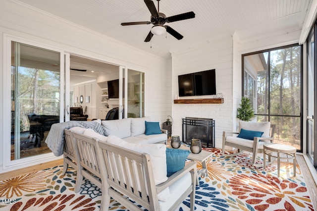 sunroom featuring a brick fireplace and a ceiling fan