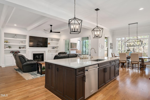 kitchen featuring dark brown cabinetry, a glass covered fireplace, light wood-type flooring, stainless steel dishwasher, and a sink