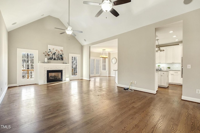 unfurnished living room with ceiling fan, high vaulted ceiling, dark wood-style flooring, a fireplace, and baseboards