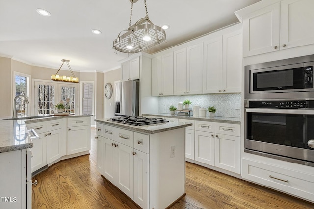 kitchen with a center island, pendant lighting, appliances with stainless steel finishes, white cabinets, and a sink