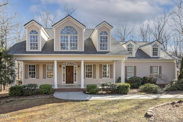 cape cod-style house featuring covered porch, a shingled roof, and a front lawn