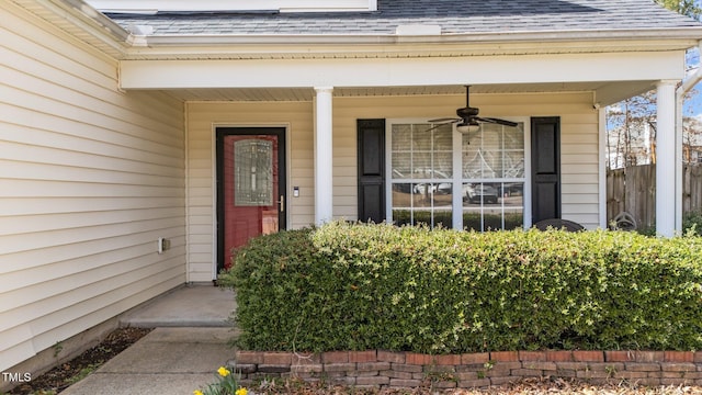 view of exterior entry with fence, a ceiling fan, and roof with shingles