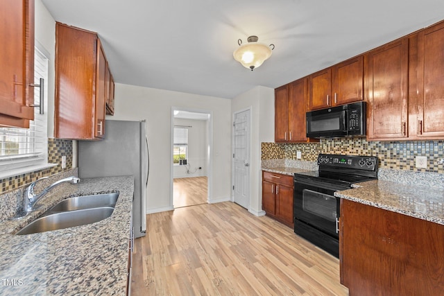 kitchen featuring a sink, light wood-type flooring, light stone countertops, black appliances, and tasteful backsplash