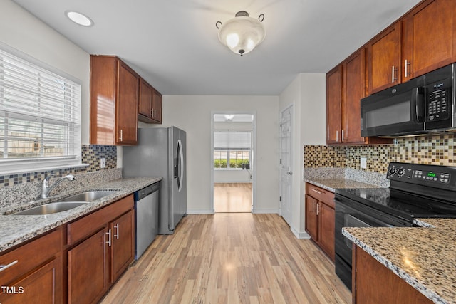 kitchen with tasteful backsplash, light wood-style flooring, light stone countertops, black appliances, and a sink