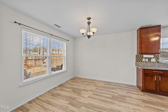 unfurnished dining area with baseboards, light wood-type flooring, visible vents, and an inviting chandelier