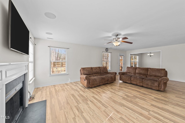 living area with visible vents, light wood-style flooring, a fireplace with flush hearth, baseboards, and ceiling fan with notable chandelier