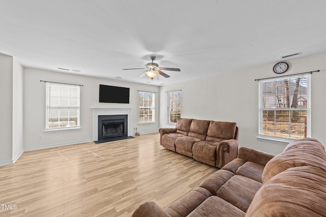 living area with baseboards, visible vents, a ceiling fan, a fireplace with flush hearth, and light wood-type flooring