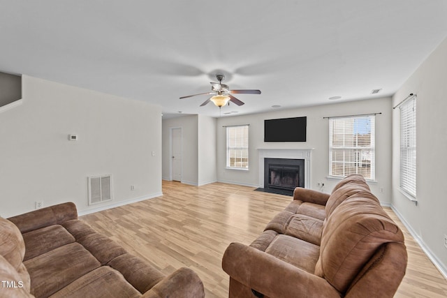 living room featuring visible vents, baseboards, a fireplace with flush hearth, ceiling fan, and light wood-style floors