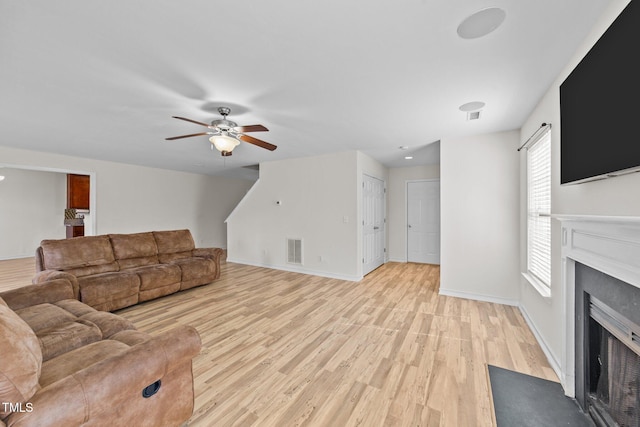 living area featuring a fireplace with flush hearth, visible vents, light wood-style floors, and baseboards