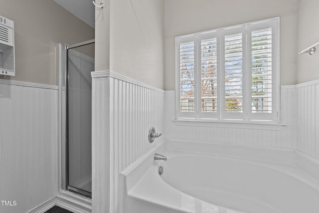 full bathroom featuring a wainscoted wall, a stall shower, and a bath