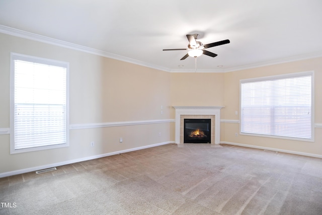 unfurnished living room with light carpet, a fireplace, a ceiling fan, baseboards, and ornamental molding