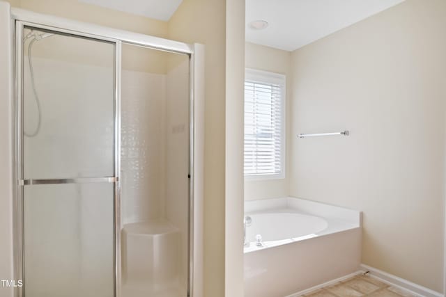 bathroom with a stall shower, a bath, and baseboards