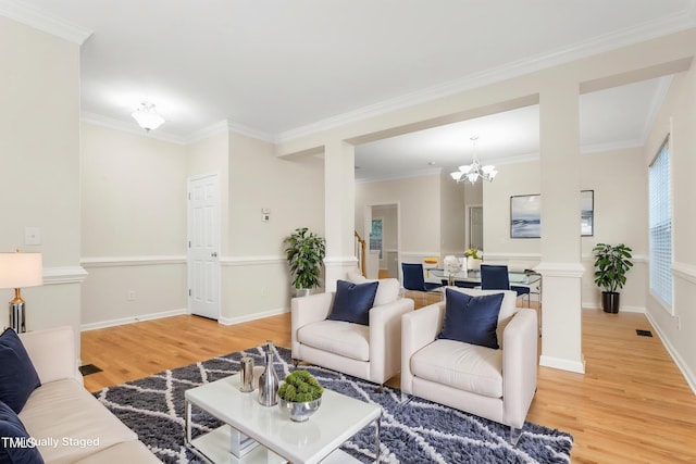 living room featuring ornate columns, light wood-type flooring, a chandelier, crown molding, and baseboards