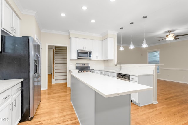kitchen featuring appliances with stainless steel finishes, a peninsula, a ceiling fan, light wood finished floors, and crown molding