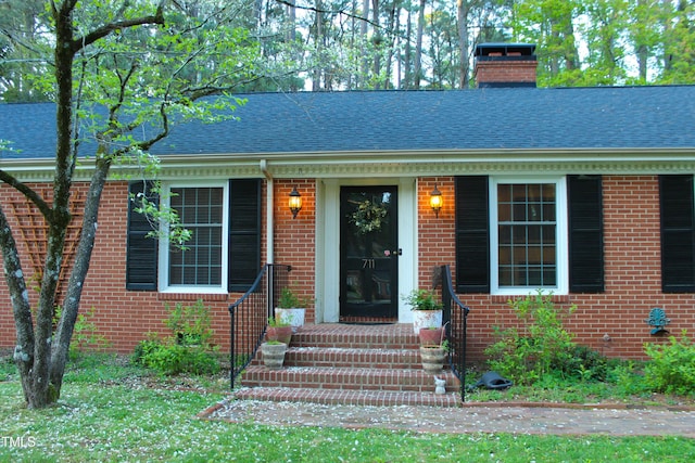 view of front of property featuring a chimney, brick siding, and roof with shingles