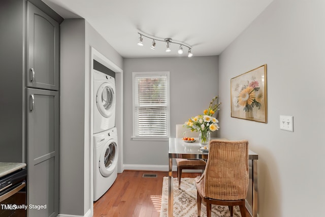 clothes washing area with light wood finished floors, stacked washer / drying machine, laundry area, visible vents, and baseboards