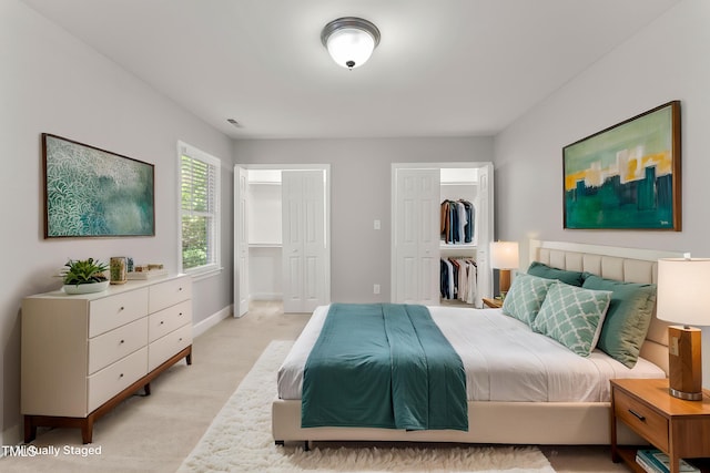 bedroom with light carpet, baseboards, visible vents, and multiple closets