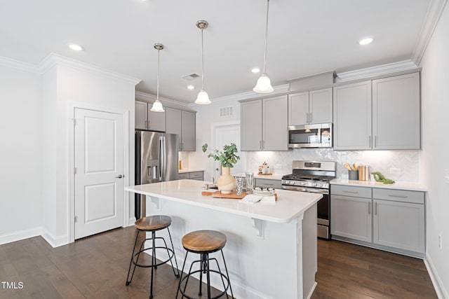 kitchen featuring a kitchen island, appliances with stainless steel finishes, a breakfast bar area, ornamental molding, and gray cabinets