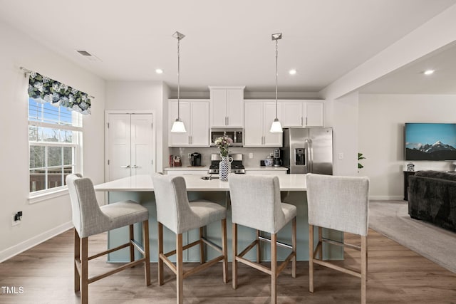 kitchen featuring a center island with sink, light countertops, appliances with stainless steel finishes, wood finished floors, and white cabinets