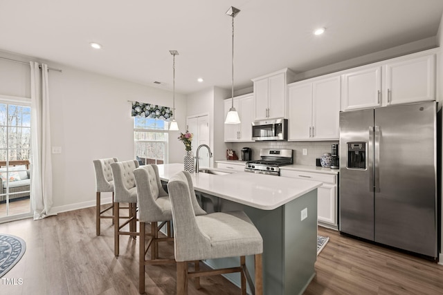 kitchen featuring dark wood-type flooring, an island with sink, a sink, appliances with stainless steel finishes, and decorative backsplash