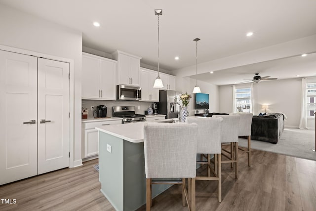 kitchen with ceiling fan, a center island with sink, appliances with stainless steel finishes, a kitchen breakfast bar, and white cabinets