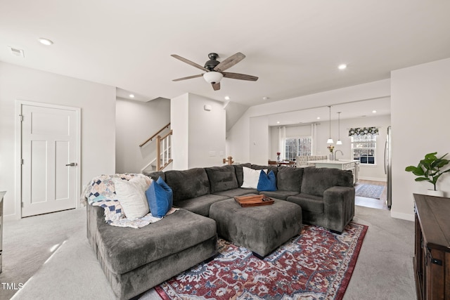 living area featuring stairway, a ceiling fan, visible vents, and light carpet