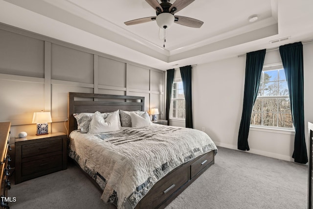 bedroom featuring a raised ceiling, a decorative wall, visible vents, and light carpet