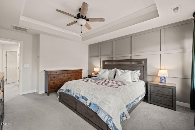 carpeted bedroom featuring a decorative wall, visible vents, and a tray ceiling