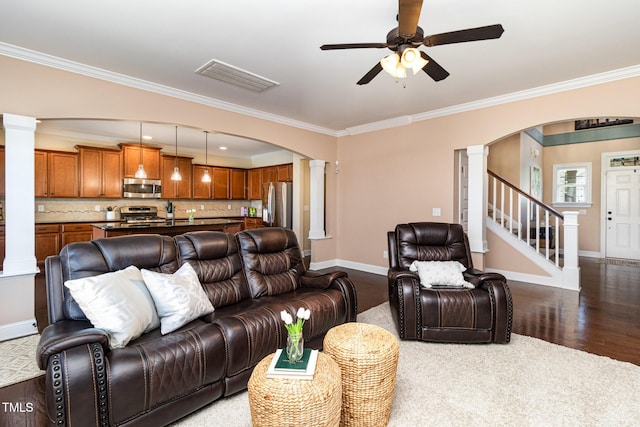 living area featuring arched walkways, ornate columns, wood finished floors, baseboards, and stairs